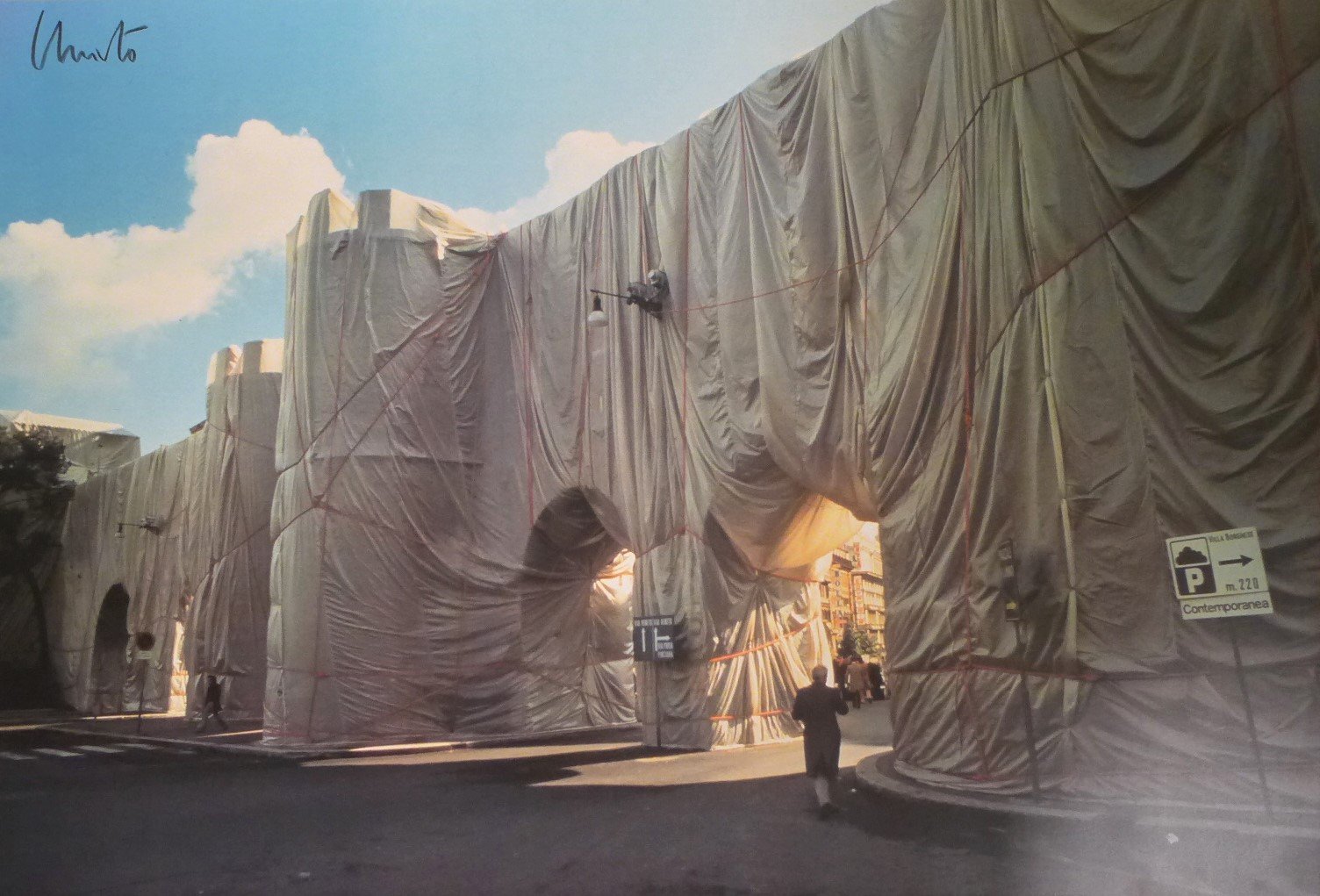 Photographie signée d'une intervention de Christo & Jeanne-Claude : un mur d'enceinte urbain entièrement emballé de toile claire et de cordes rouges